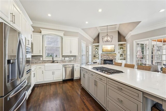 kitchen featuring crown molding, appliances with stainless steel finishes, a fireplace, a notable chandelier, and a sink