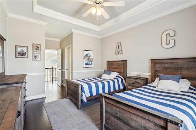 bedroom with ornamental molding, a tray ceiling, wood finished floors, baseboards, and ceiling fan