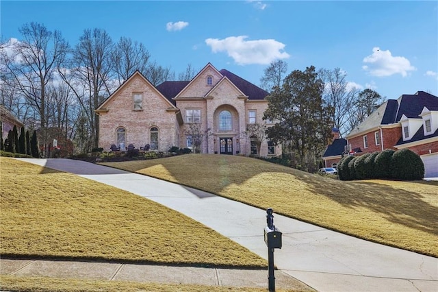 french country style house with brick siding and a front lawn