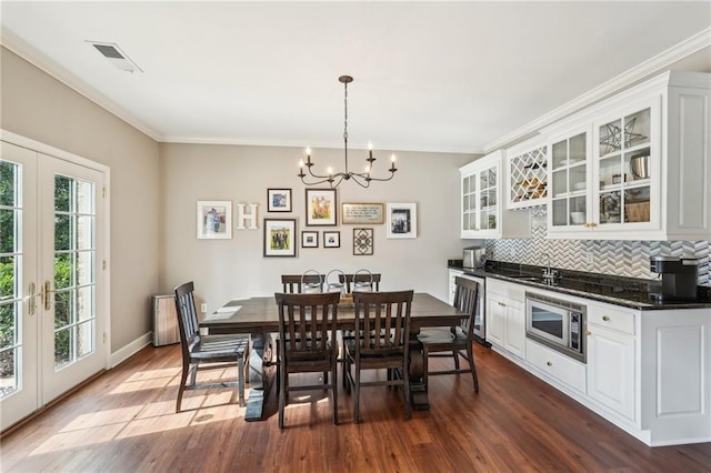 dining area featuring a notable chandelier, visible vents, crown molding, and dark wood-style floors