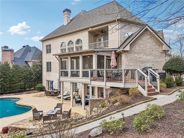 rear view of house featuring a patio, a balcony, a sunroom, a chimney, and brick siding