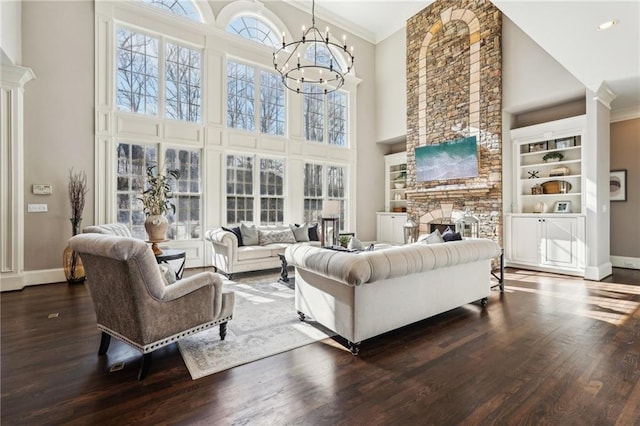 living room featuring a stone fireplace, a healthy amount of sunlight, wood finished floors, and a chandelier