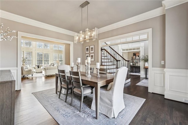 dining area featuring dark wood-style floors, a wainscoted wall, stairway, and crown molding