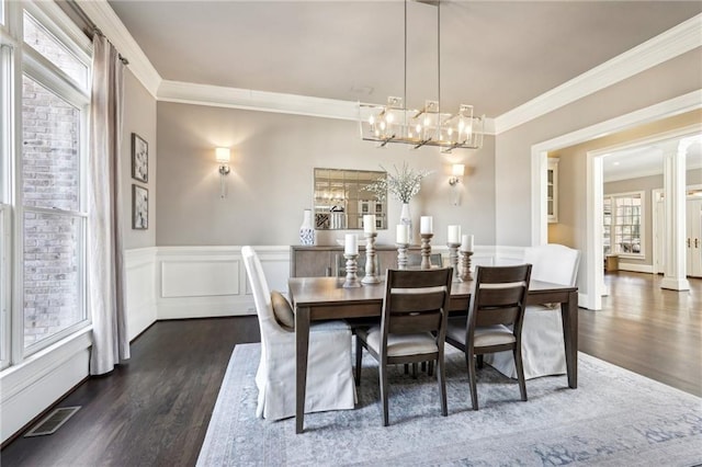 dining space featuring wainscoting, dark wood-type flooring, an inviting chandelier, and ornamental molding