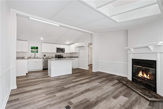 kitchen with white cabinetry, appliances with stainless steel finishes, hardwood / wood-style flooring, and a kitchen island