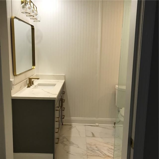 half bathroom featuring marble finish floor, baseboards, vanity, and toilet