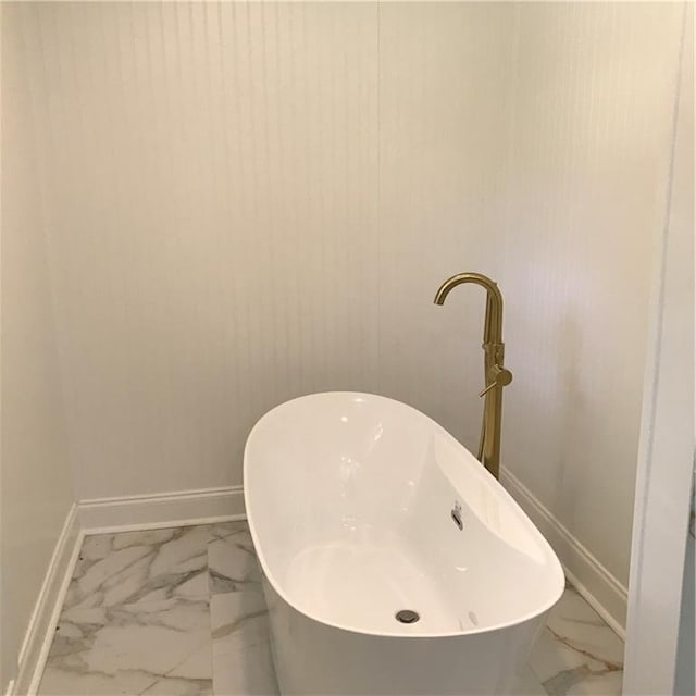 full bathroom with marble finish floor, a freestanding tub, and baseboards