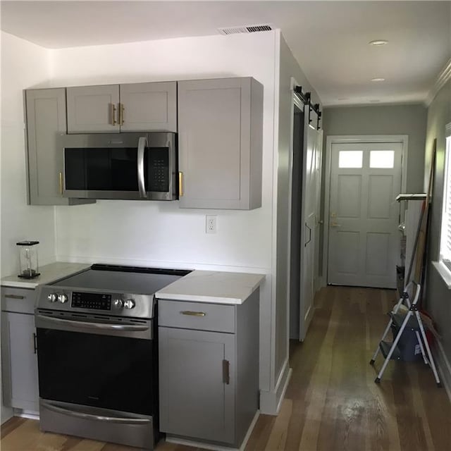 kitchen featuring visible vents, gray cabinetry, a barn door, appliances with stainless steel finishes, and wood finished floors