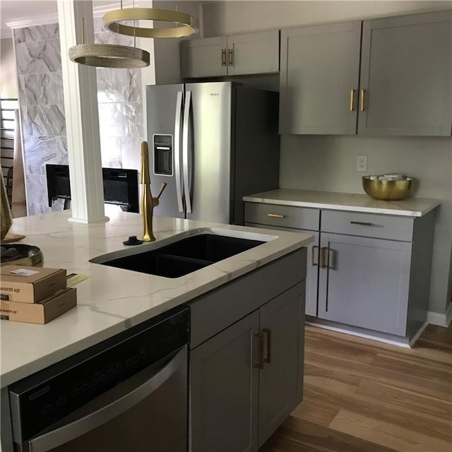 kitchen featuring gray cabinetry, stainless steel appliances, a sink, light wood-style floors, and light stone countertops