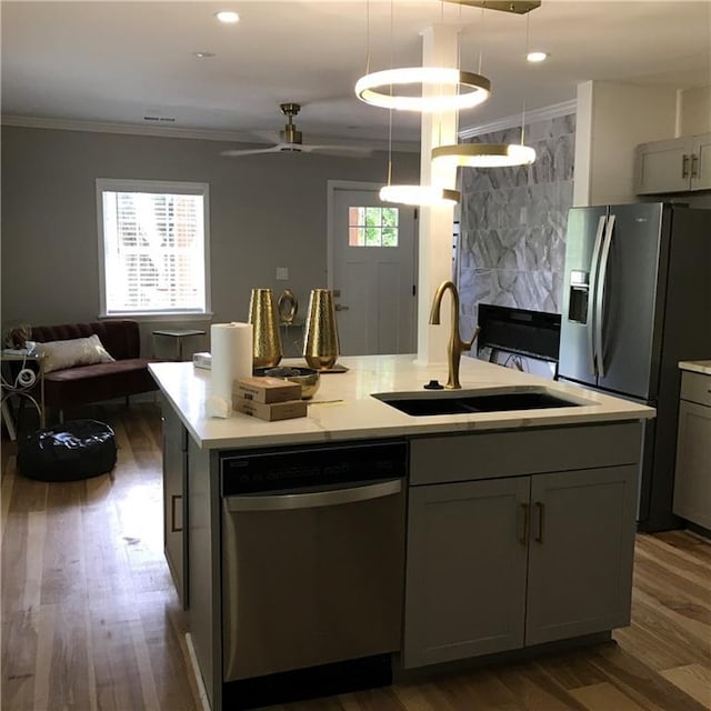 kitchen featuring a center island with sink, appliances with stainless steel finishes, ornamental molding, light countertops, and a sink