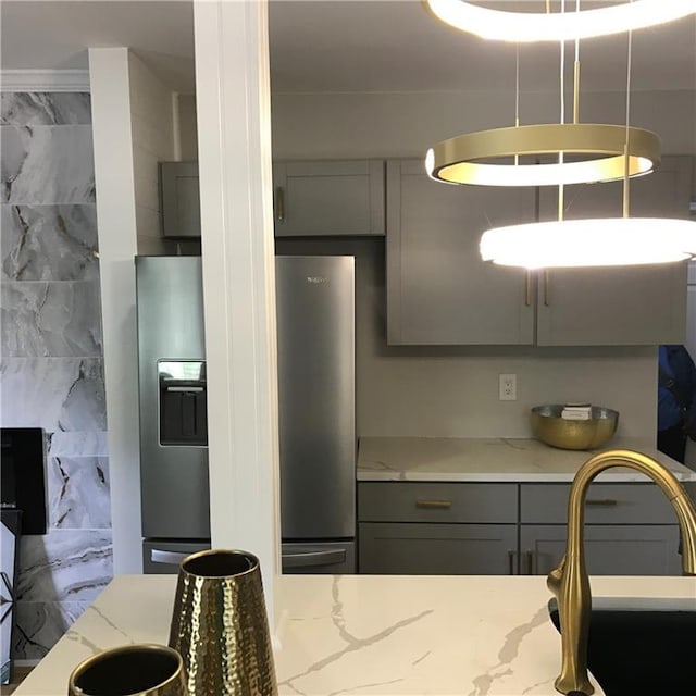 kitchen featuring light stone counters, gray cabinetry, freestanding refrigerator, a sink, and stainless steel fridge