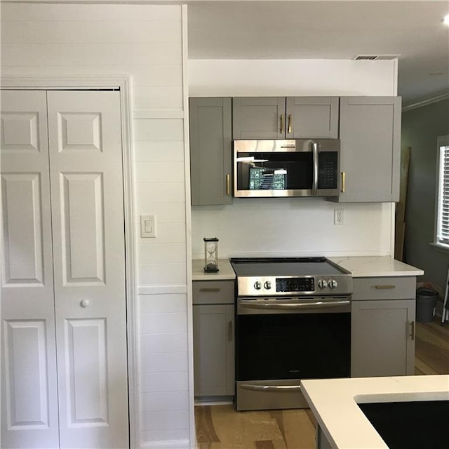 kitchen featuring crown molding, stainless steel appliances, light countertops, and gray cabinetry