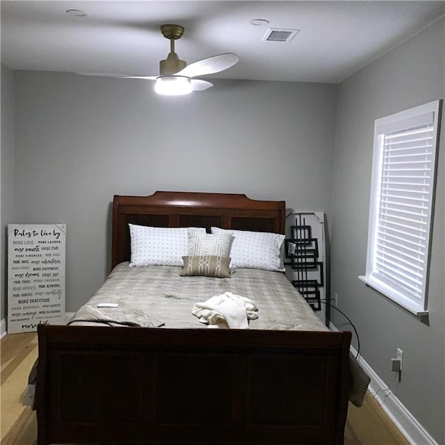 bedroom featuring ceiling fan, visible vents, baseboards, and wood finished floors