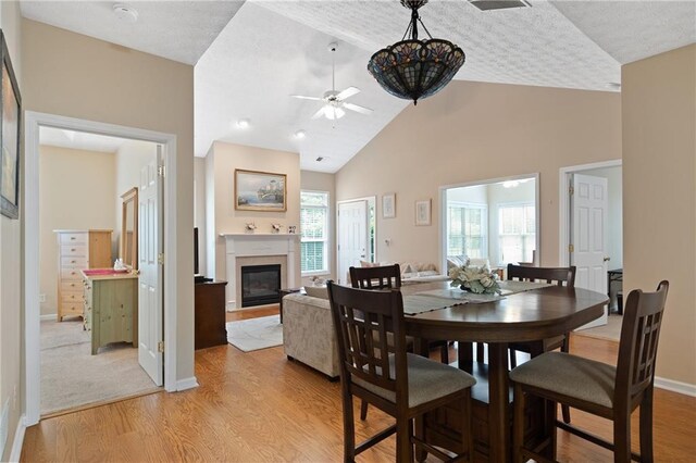 3734 Villa Springs Cir, Powder Springs, GA 30127 - dining space featuring a glass covered fireplace, light wood-type flooring, ceiling fan, baseboards, and high vaulted ceiling