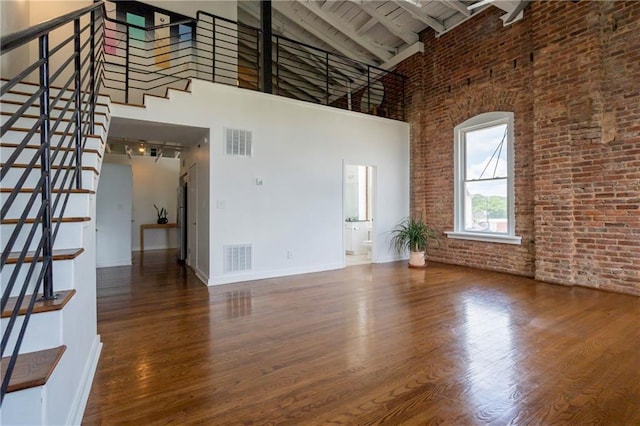 1596 Cleveland Ave Unit 301, East Point, GA 30344 - unfurnished living room with a towering ceiling, wood finished floors, stairway, beamed ceiling, and brick wall