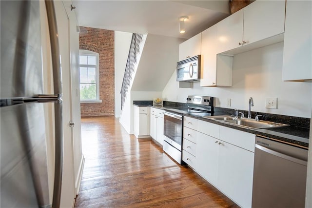 1596 Cleveland Ave Unit 301, East Point, GA 30344 - kitchen with appliances with stainless steel finishes, dark countertops, dark wood-style floors, brick wall, and white cabinets