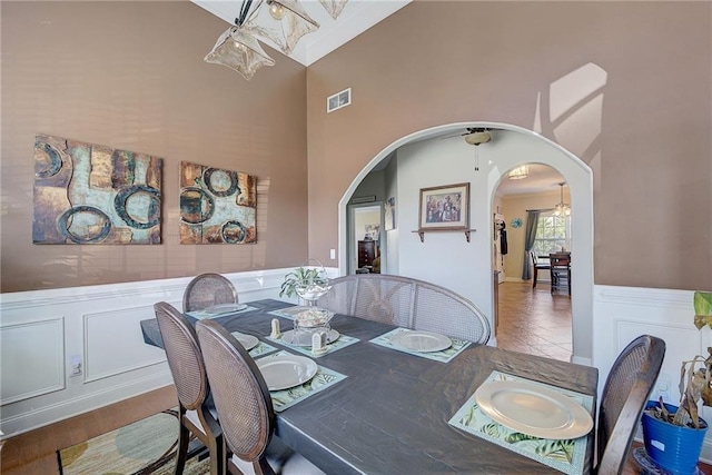 dining space with arched walkways, a decorative wall, a wainscoted wall, a high ceiling, and visible vents