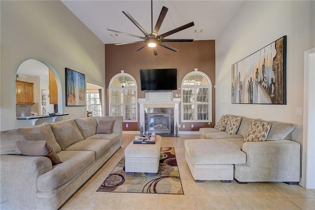 living room featuring a high end fireplace, light tile patterned flooring, ceiling fan, high vaulted ceiling, and baseboards