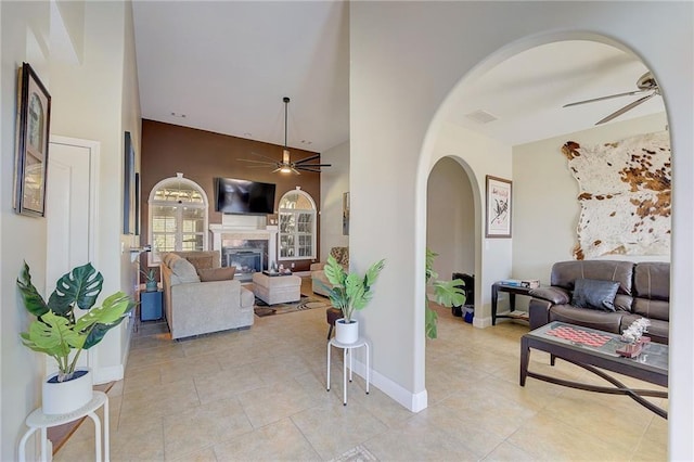 living room featuring light tile patterned floors, visible vents, arched walkways, a ceiling fan, and a fireplace