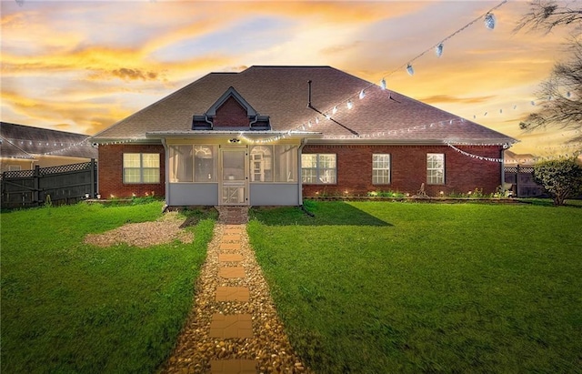 exterior space with a shingled roof, a sunroom, fence, a yard, and brick siding