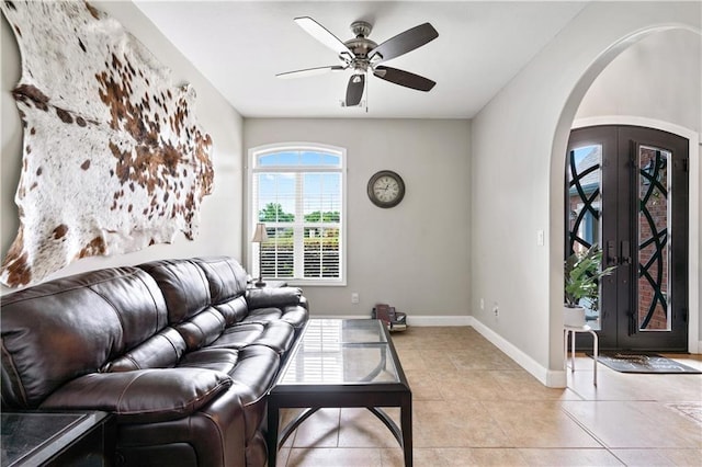 living room with arched walkways, french doors, a ceiling fan, light tile patterned flooring, and baseboards