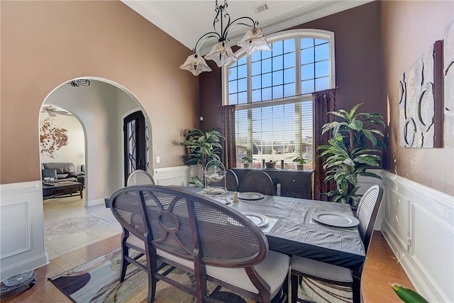 dining space with arched walkways, a wainscoted wall, and a chandelier