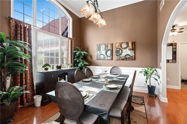 dining space featuring arched walkways, hardwood / wood-style flooring, a high ceiling, visible vents, and crown molding