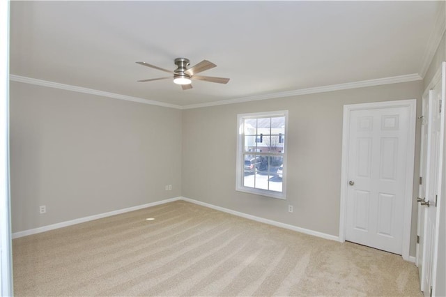 spare room featuring light carpet, ceiling fan, crown molding, and baseboards