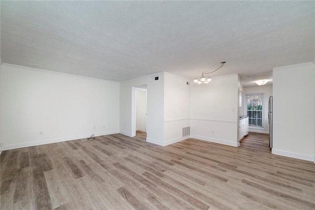 empty room featuring a textured ceiling, light hardwood / wood-style flooring, an inviting chandelier, and ornamental molding