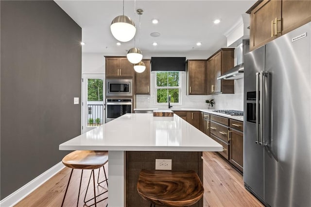 kitchen featuring a kitchen bar, backsplash, stainless steel appliances, light wood-style floors, and light countertops