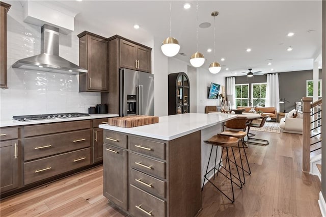 kitchen with dark brown cabinets, a kitchen bar, appliances with stainless steel finishes, and wall chimney range hood