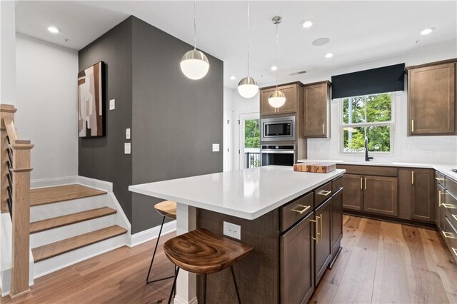 kitchen with light wood finished floors, a kitchen breakfast bar, a kitchen island, stainless steel appliances, and light countertops