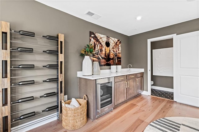 bar featuring visible vents, baseboards, beverage cooler, light wood-type flooring, and a sink