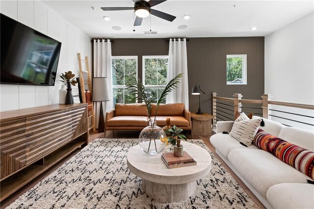 living room with a wealth of natural light, visible vents, wood finished floors, and a ceiling fan