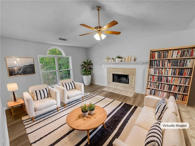 living area featuring a ceiling fan, visible vents, a fireplace with flush hearth, wood finished floors, and lofted ceiling