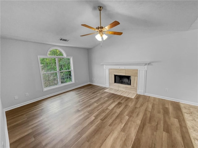 unfurnished living room with ceiling fan, visible vents, wood finished floors, a tile fireplace, and lofted ceiling