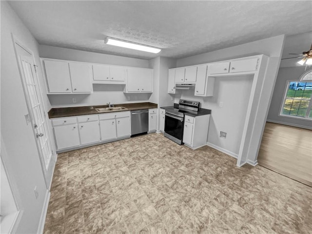 kitchen with dark countertops, a sink, stainless steel appliances, white cabinetry, and light floors