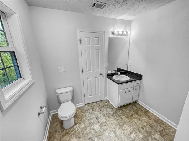 half bathroom featuring vanity, toilet, a textured ceiling, and visible vents