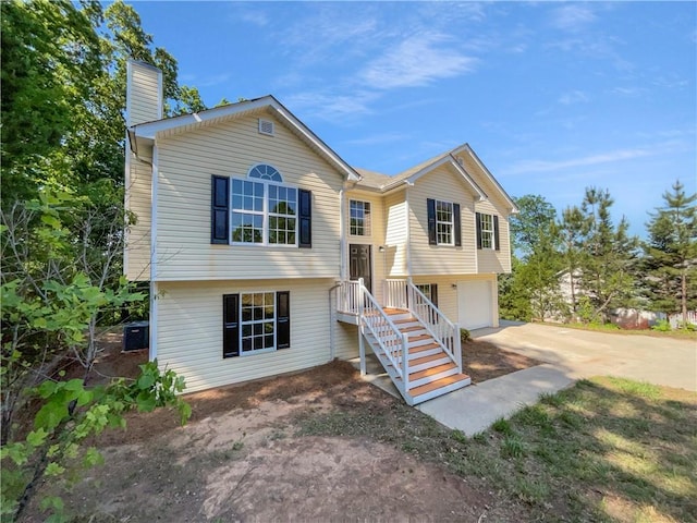 split foyer home featuring central AC unit, a chimney, an attached garage, and driveway