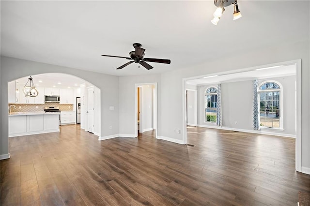 unfurnished living room featuring dark wood-type flooring, baseboards, arched walkways, and ceiling fan