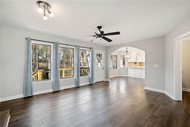 unfurnished living room featuring dark wood-style floors, visible vents, baseboards, arched walkways, and ceiling fan with notable chandelier