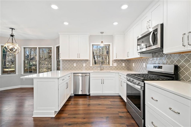 kitchen with a sink, stainless steel appliances, a peninsula, light countertops, and dark wood-style flooring