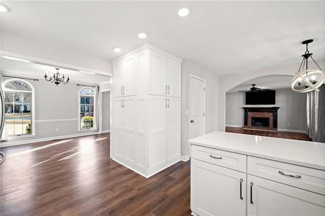 kitchen with arched walkways, dark wood-style flooring, white cabinetry, a brick fireplace, and open floor plan