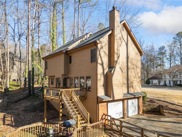 rear view of property featuring a chimney, a deck, fence, concrete driveway, and stairs