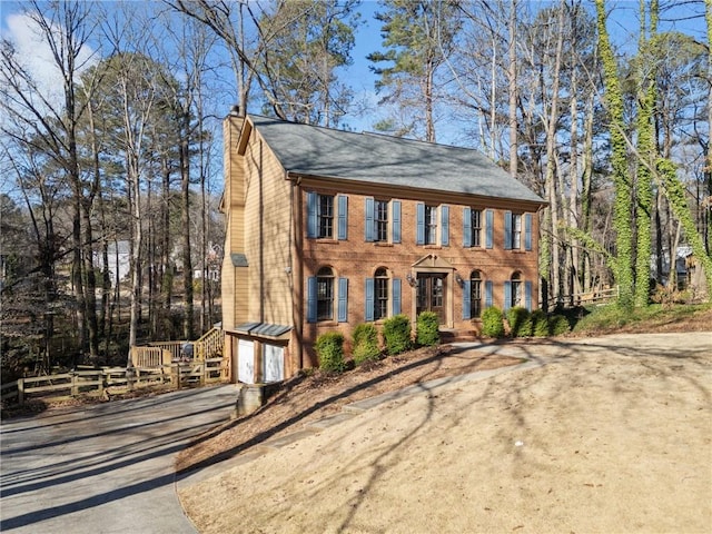 colonial home featuring a garage, brick siding, a chimney, and driveway