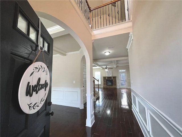 foyer featuring a stone fireplace, coffered ceiling, ceiling fan, dark wood-type flooring, and beam ceiling