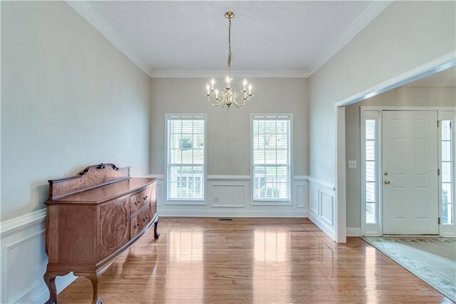 interior space featuring an inviting chandelier, ornamental molding, wainscoting, and wood finished floors