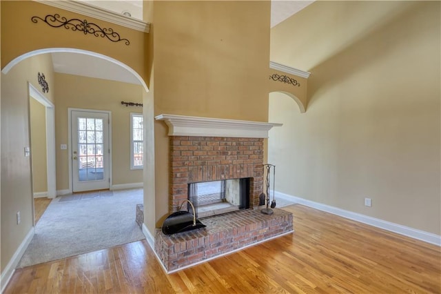 unfurnished living room featuring arched walkways, a high ceiling, a brick fireplace, wood finished floors, and baseboards