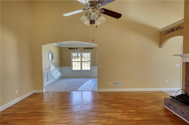 unfurnished living room featuring visible vents, a wainscoted wall, wood finished floors, a brick fireplace, and a decorative wall