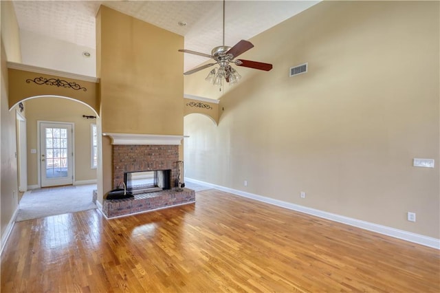 unfurnished living room with a fireplace, visible vents, a high ceiling, wood finished floors, and baseboards